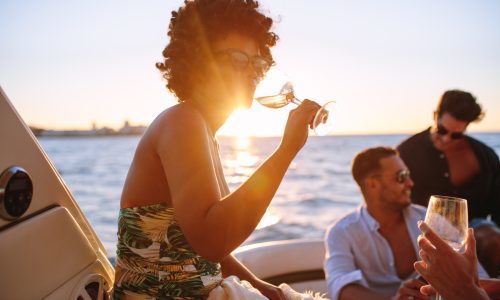 African woman drinking during sunset boat party with friends. Group of men and women having a boat party during sunset.